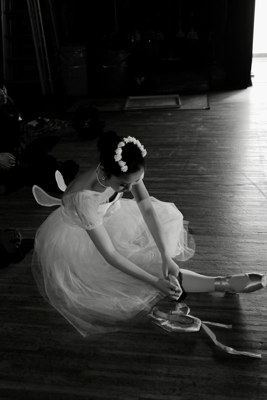 A ballerina tying her pointe shoe before a performance